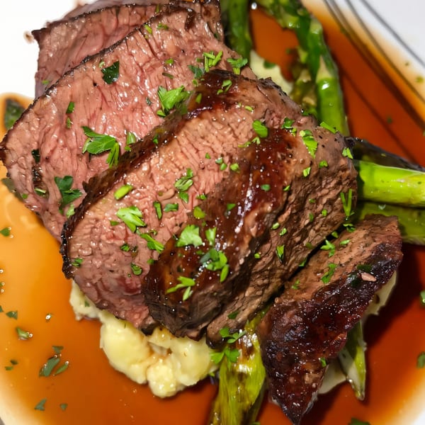 Sliced steak with gravy, mashed potatoes, and asparagus on a white plate at The Hive Bar & Bistro.