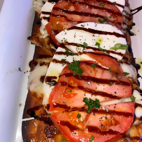 Caprese flatbread with sliced tomatoes, mozzarella, balsamic glaze, and herbs on a white plate.