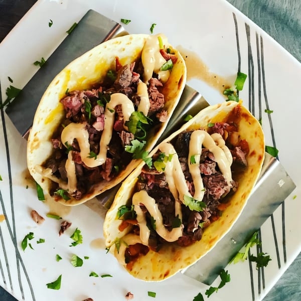 Two steak tacos with creamy sauce and cilantro, served on a white plate at The Hive Bar & Bistro.