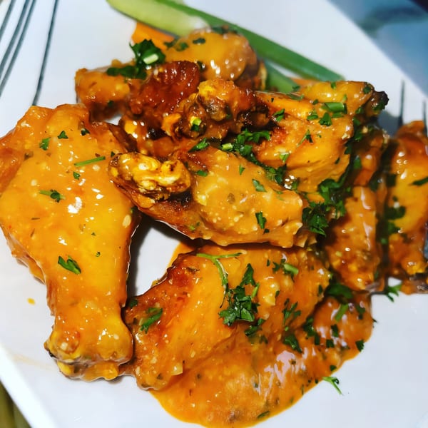 A plate of The Hive Bar & Bistro's chicken wings, coated in orange sauce and garnished with parsley.